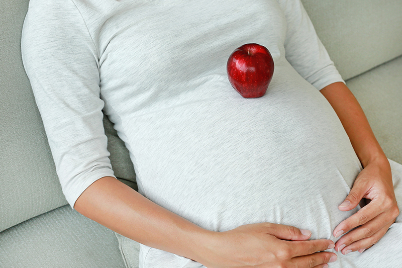 Schwangere mit Apfel auf Bauch